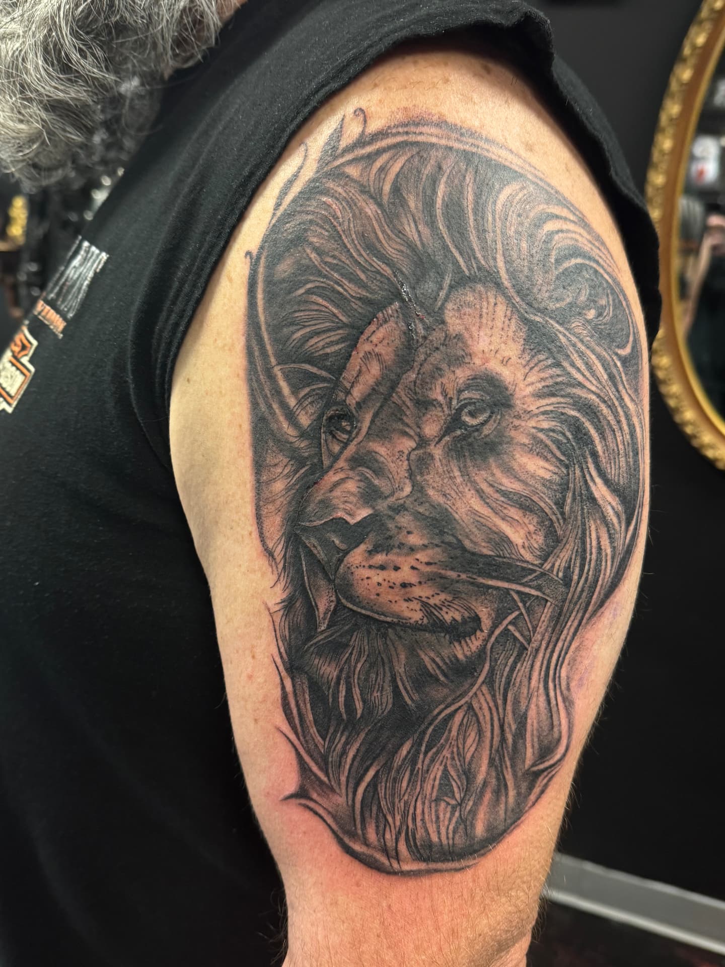 Black and grey lion portrait on an upper arm with flowing mane and grasses