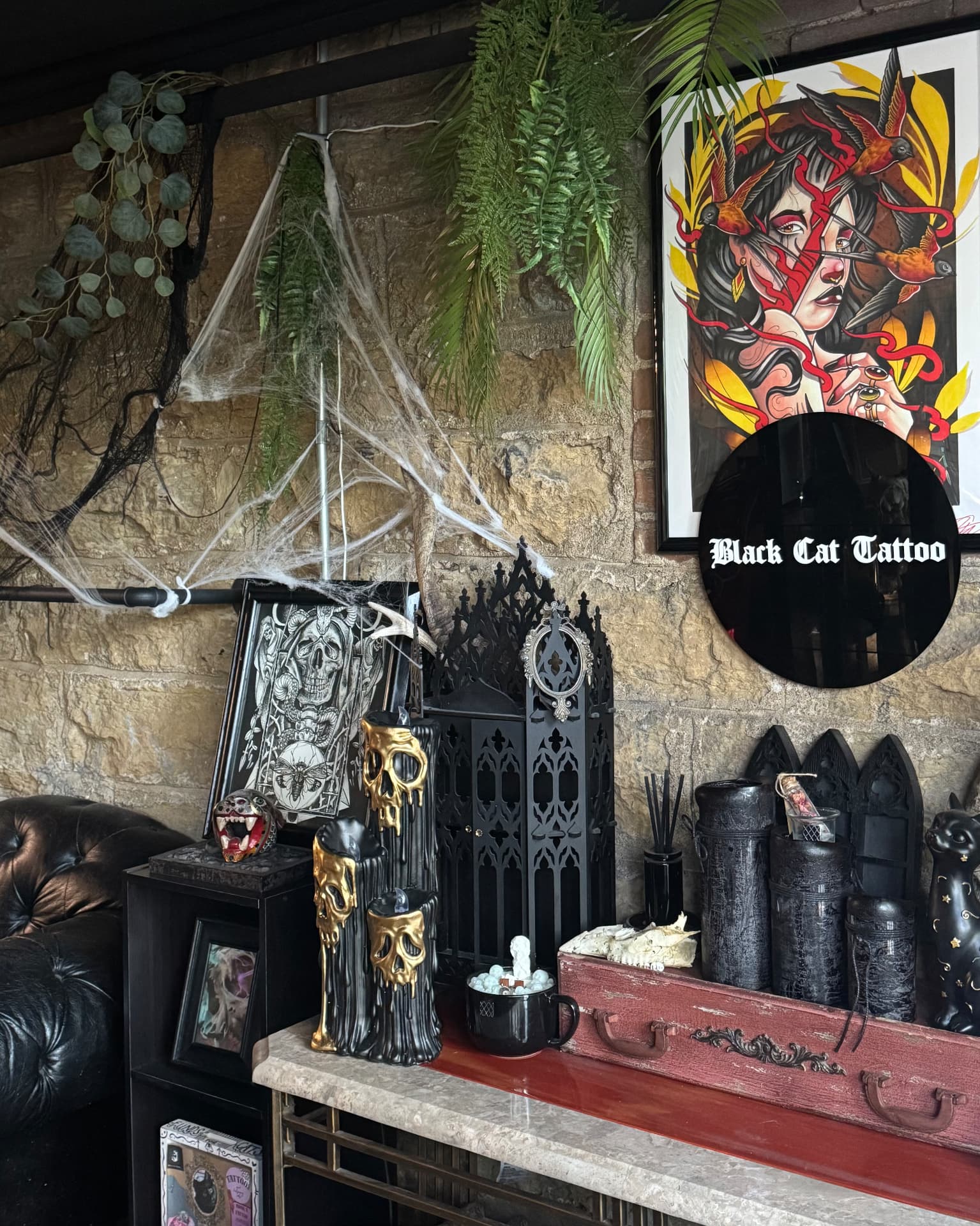 Stone-walled studio corner with skulls, cobwebs and the Black Cat Tattoo sign